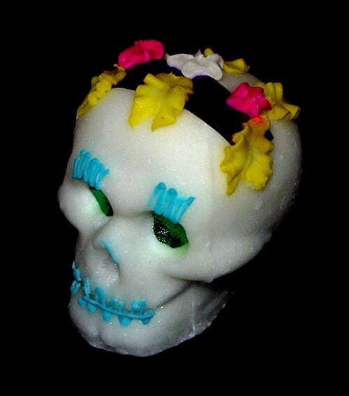 A hand-painted sugar skull with marigold decorations, colored icing patterns, and a name written across the forehead