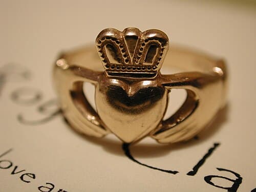 A gold Claddagh ring showing two hands holding a crowned heart, the classic Irish design