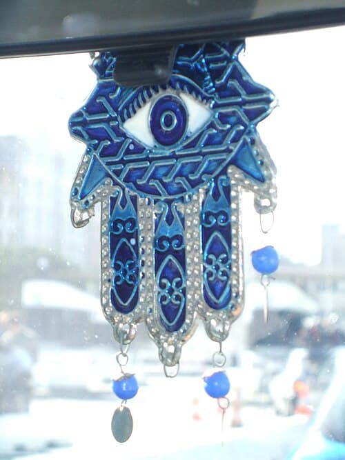 Gold hamsa hand amulet with blue evil eye in center palm